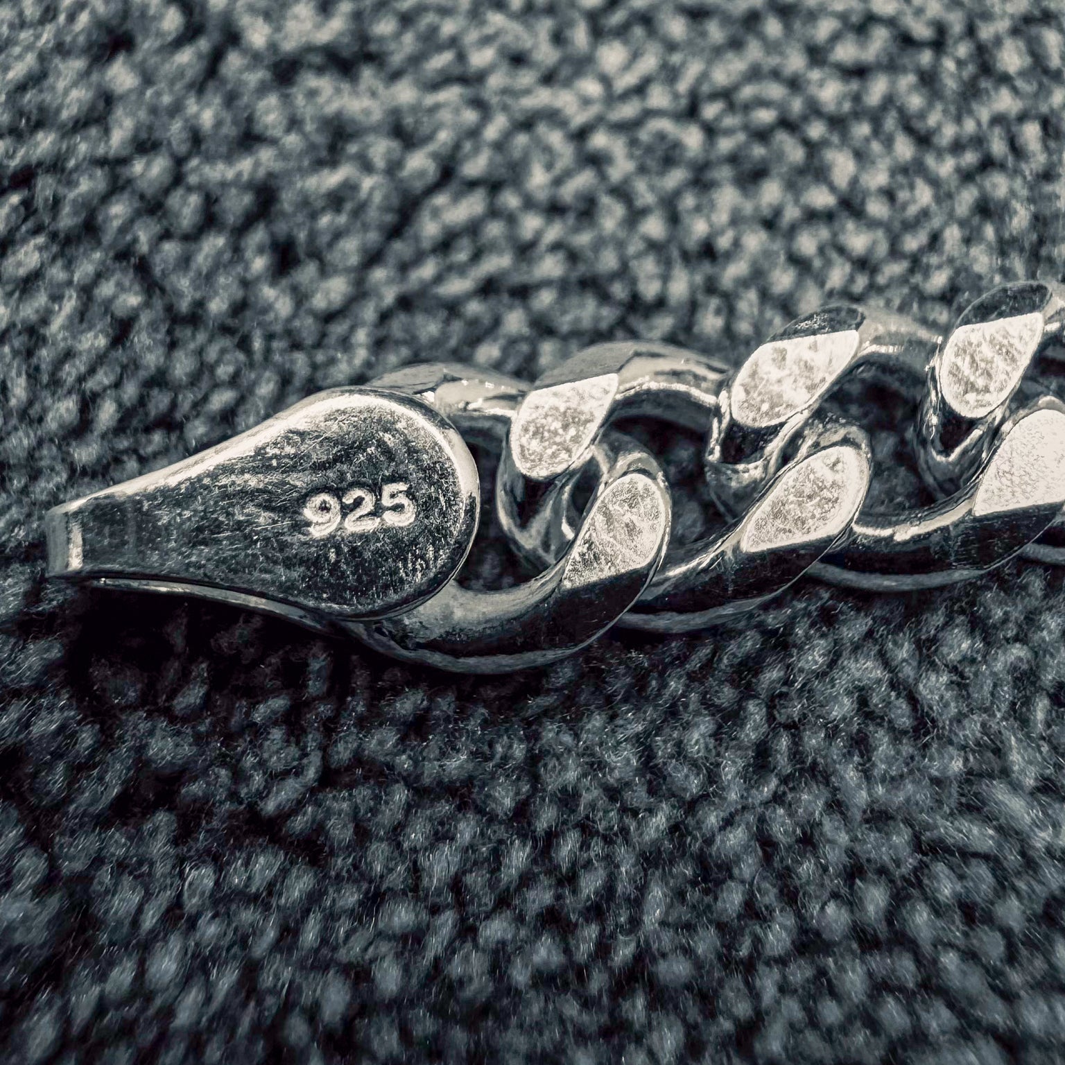 Close-up of a silver chain with '925' stamp on a textured surface