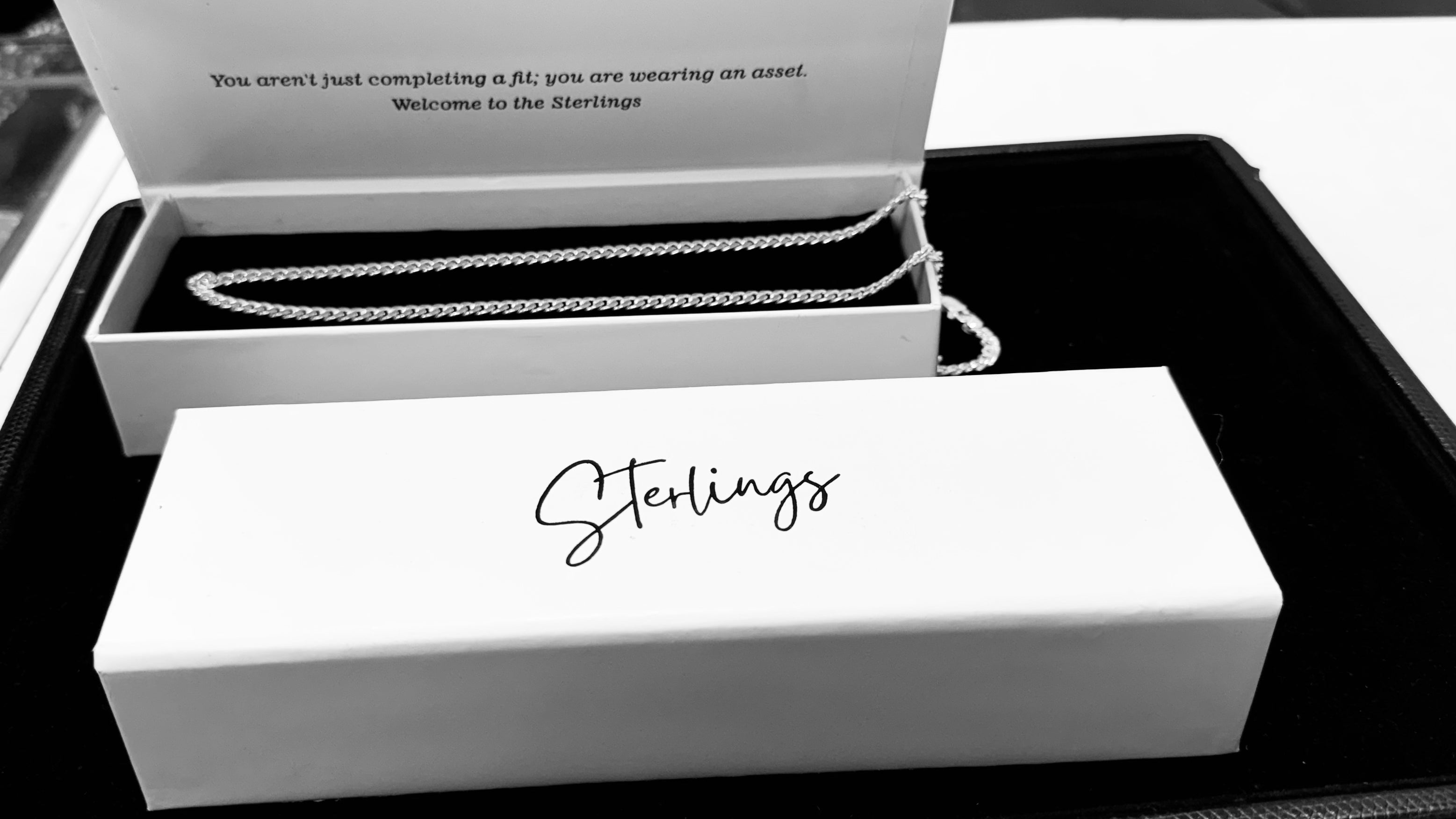 A silver chain necklace displayed inside an open white jewelry box with the brand name 'Sterlings' printed on the lid, alongside a closed white Sterling's gift box in the foreground.