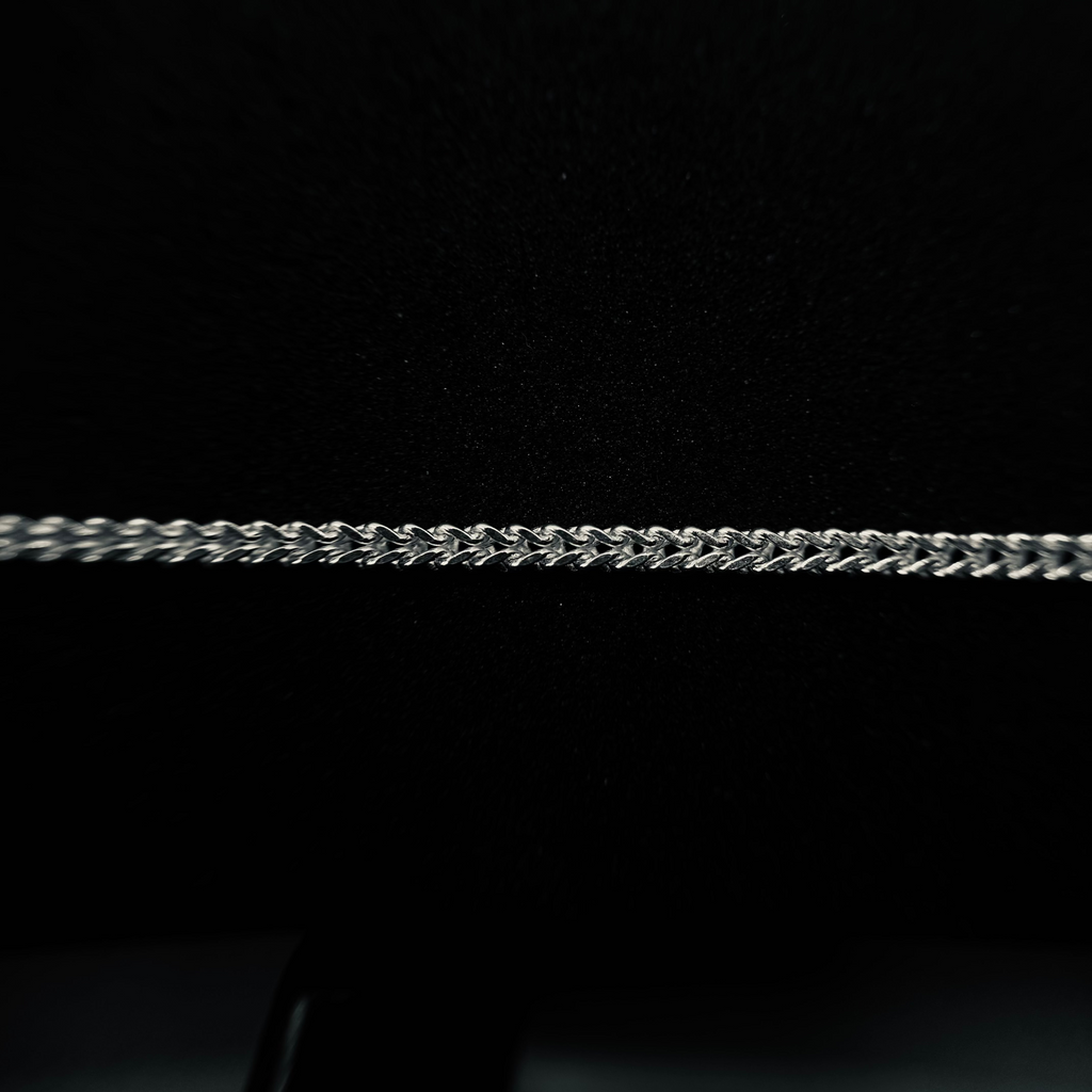 A close-up of a silver-toned curb chain necklace laid horizontally against a solid black background.