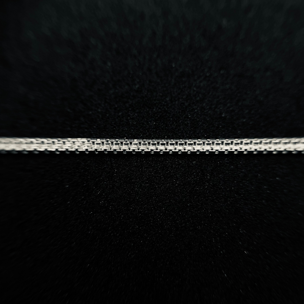 A close-up of a silver chain necklace laid horizontally against a textured black background.