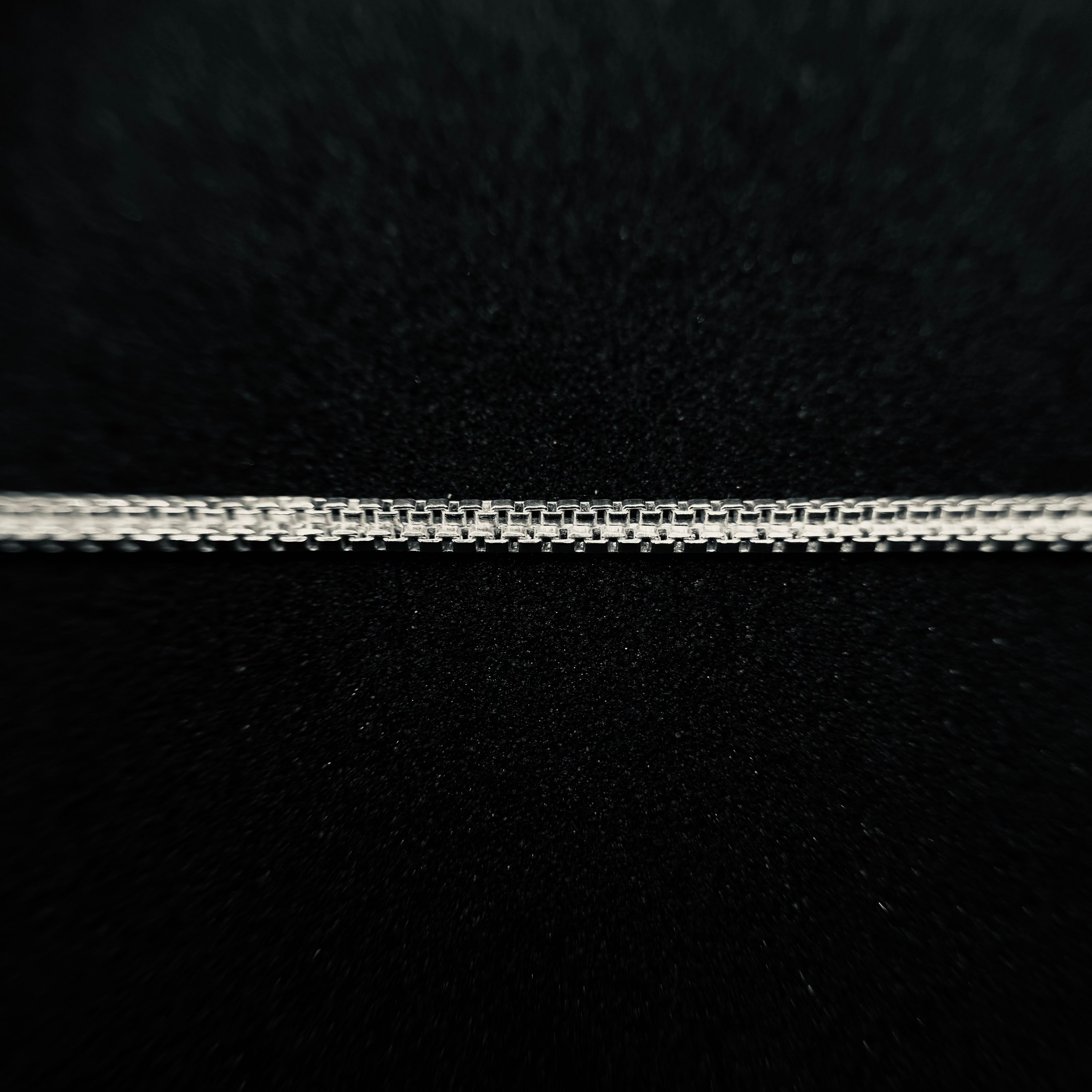 A close-up of a silver chain necklace laid horizontally against a textured black background.